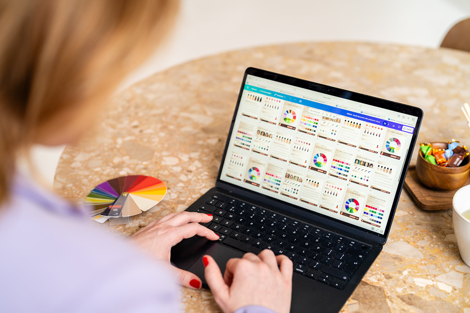Marly analyseert kleurmaterialen op haar laptop, met de kleurenwaaier naast zich